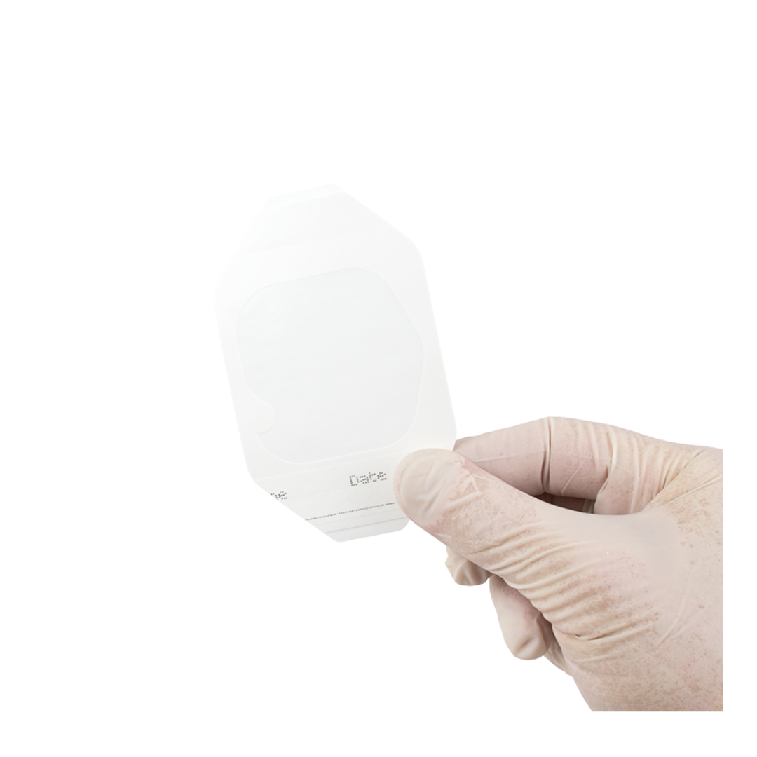 A gloved hand holds a Dynarex Transparent Film Dressing Frame Style with a white backing, ideal for wound protection or as a catheter site dressing, against a white background.